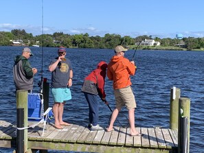 A wooden dock extending into a body of water with four people fishing.