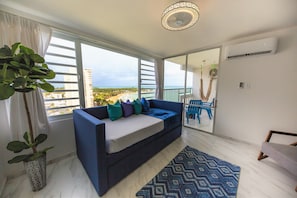 Relax in this stylish living room with a sofa, rug, and potted plant, offering a view of the beach and surrounding buildings.
