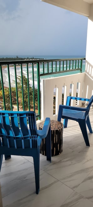 Enjoy the ocean view from this balcony with two chairs and a table.