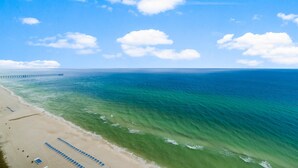 Une plage avec une jetée qui s’avance dans l’océan, un ciel dégagé et une eau calme.