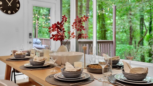 Une table à manger dressée avec des assiettes, des bols, des verres et un vase contenant des feuilles rouges.