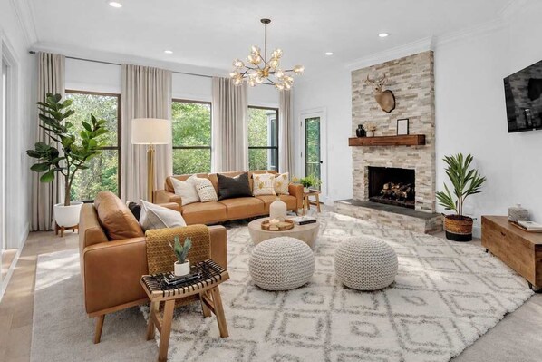 A modern living room with a fireplace, leather sofa, and a large window. - Indoor Playground + Game Room | Hot Tub | 7BR |Stone Mtn (Stone Mountain)
