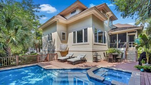 A two-story house with a swimming pool, outdoor furniture, and tropical plants. - PRIVATE Beach access, 4th Row, Heated Pool & Dog Friendly (Hilton Head Island)