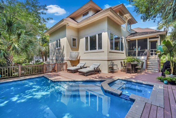 A two-story house with a swimming pool, outdoor furniture, and tropical plants.