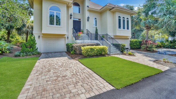 A two-story house with a brick driveway, a front lawn, and a staircase leading to a balcony.