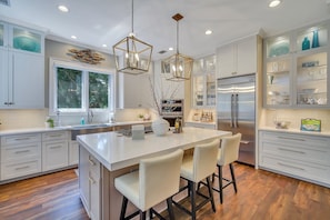 A modern kitchen with white cabinetry, a central island with stools, stainless steel appliances, and pendant lighting.