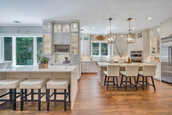 A modern kitchen with a large island, bar stools, and a dining area with a view of the outdoors.