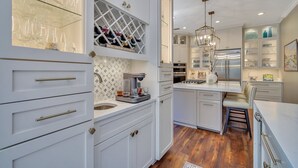 A modern kitchen with white cabinetry, a built-in wine rack, a coffee machine, and a stainless steel refrigerator.