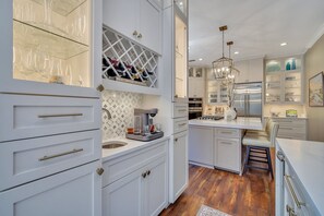 A modern kitchen with white cabinetry, a built-in wine rack, a coffee machine, and a stainless steel refrigerator.