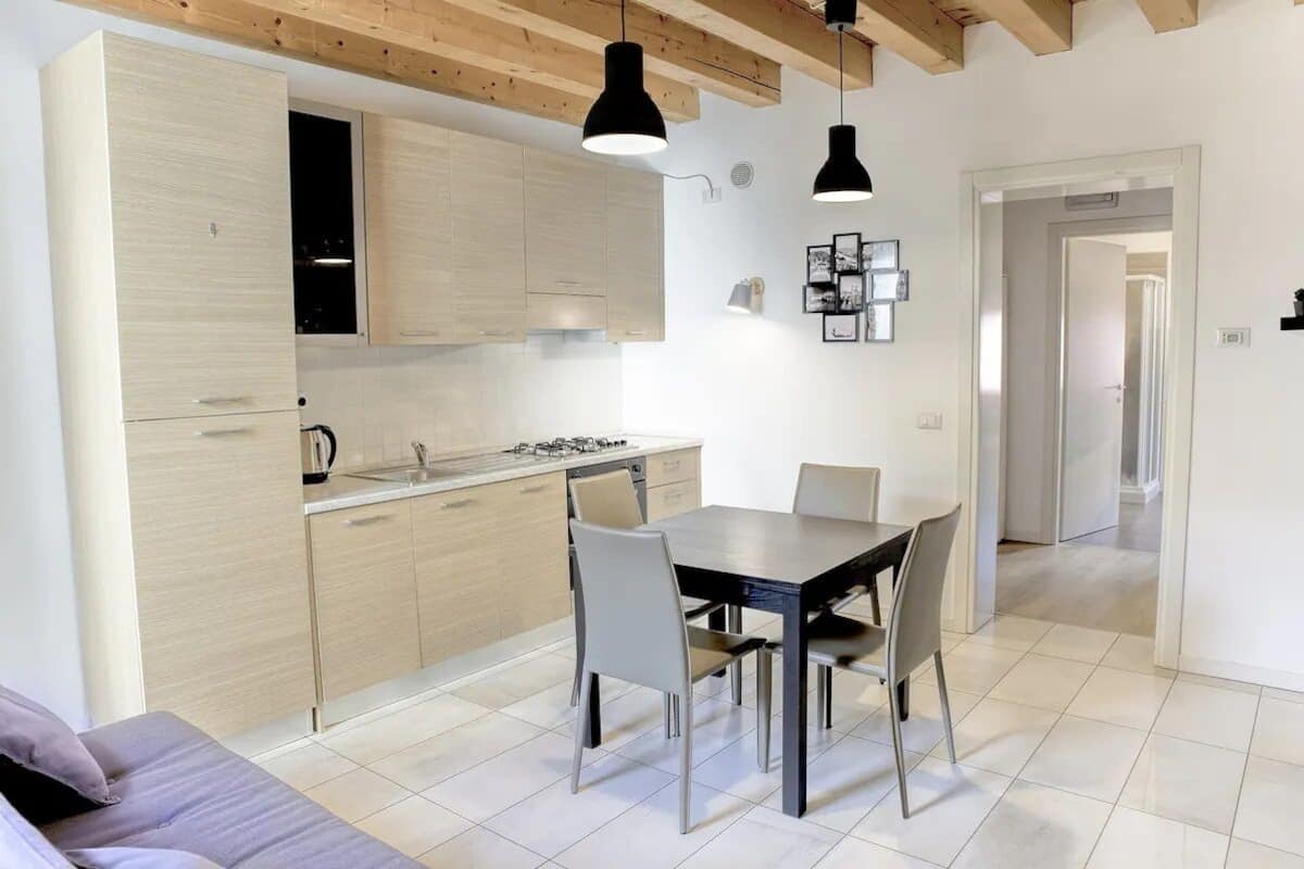 A modern kitchen with light wood cabinets, a dining table with chairs, and pendant lighting.