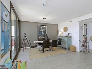 A modern living room with a dining area, a large window, and a framed artwork on the wall.