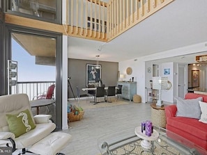 A spacious living area with a balcony, a dining area, and a red sofa.
