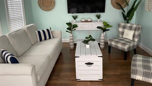Ein Wohnzimmer mit einer Couch, einem Sessel, einem Couchtisch und einem Fernseher auf einem Schrank.