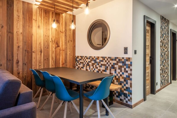 Een eethoek met een houten wand, een betegelde spatwand en een ronde spiegel boven een tafel met blauwe stoelen.