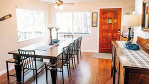 A dining area with a wooden table and chairs, a ceiling fan, and a red door.