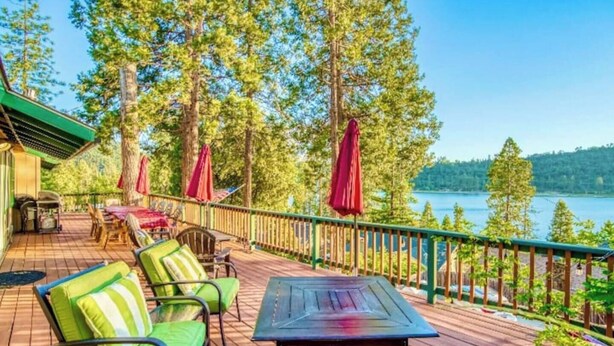 A wooden deck with outdoor seating, a view of a lake, and a forested area.