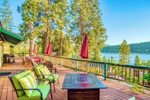 Una terraza de madera con mobiliario exterior, vista a un lago y zona boscosa.