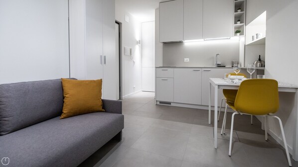 Un espacio habitable moderno y compacto con un sofá gris, un sillón amarillo y una pequeña mesa de comedor.