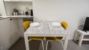 Ein kleiner Essbereich mit einem weißen Tisch, zwei gelben Stühlen und einem kleinen Fernseher auf einem weißen Schrank.