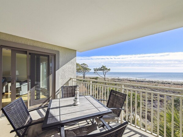 A balcony with a table and chairs, overlooking a beach.