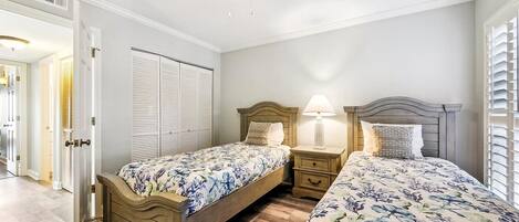 Een slaapkamer met twee bedden, een plafondventilator en een nachtkastje met een lamp.