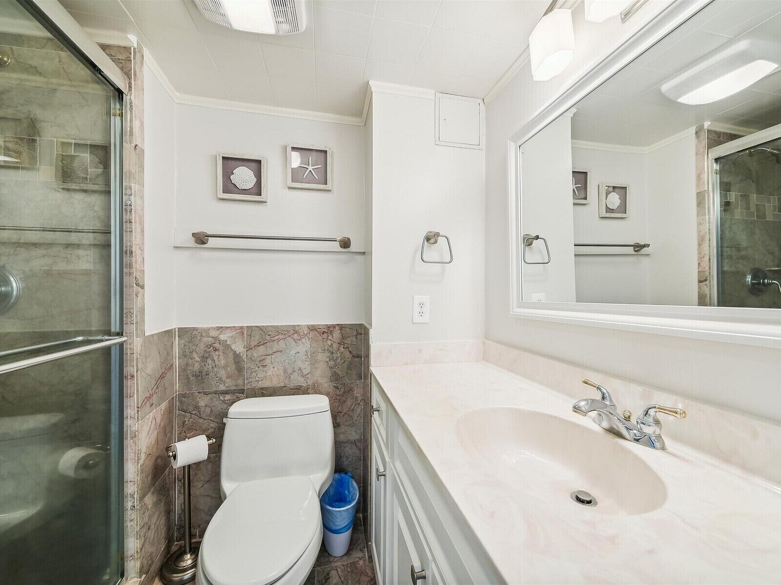 Un baño con inodoro, lavabo y ducha. Hay cuadros enmarcados en la pared y un perchero para toallas.
