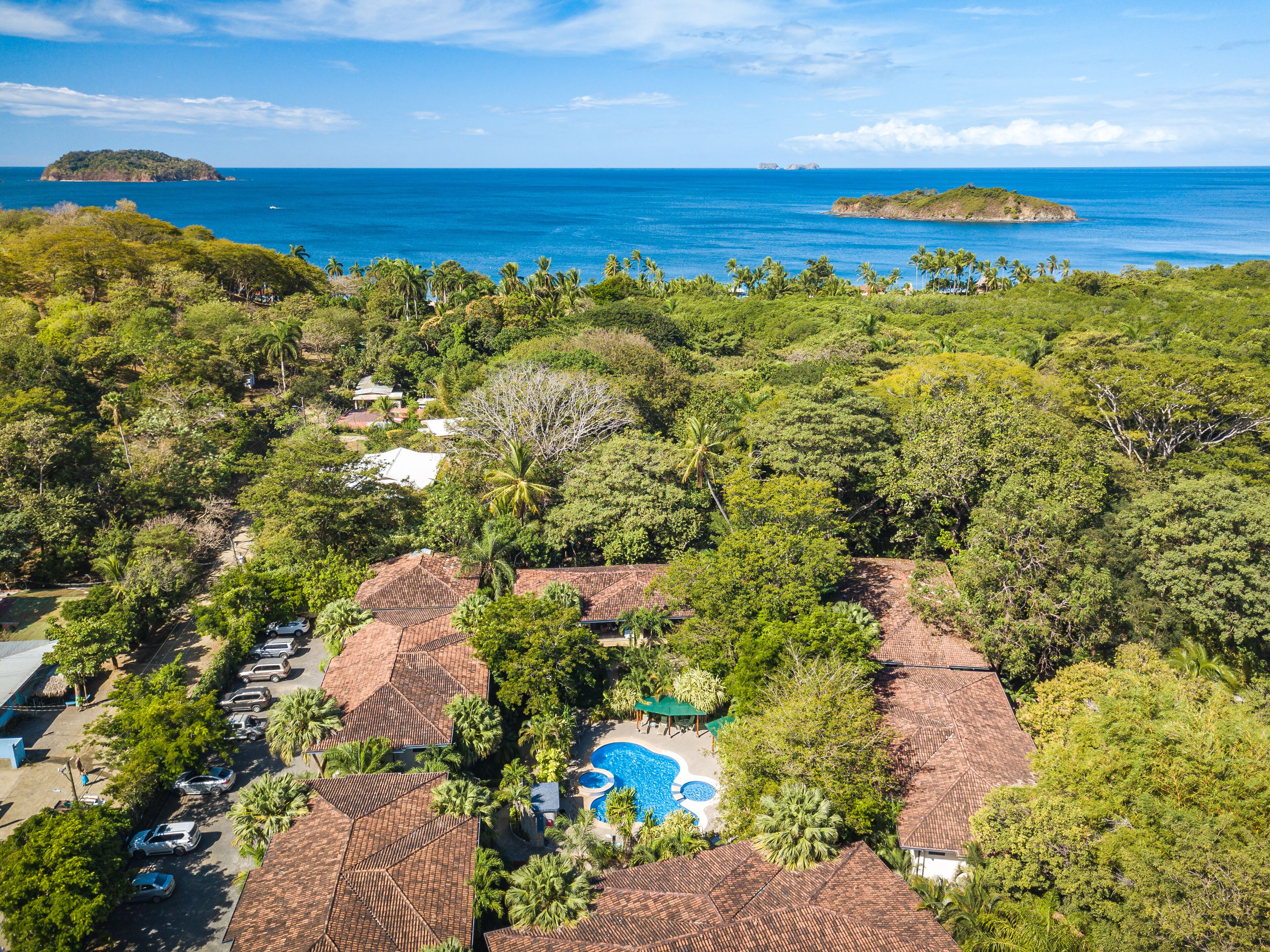 A resort with multiple bungalow-style buildings, a swimming pool, and a view of the ocean and islands.