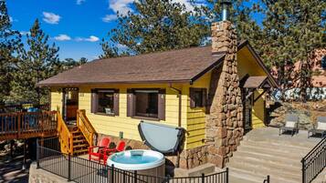 A yellow building with a stone chimney, a hot tub, and outdoor seating.