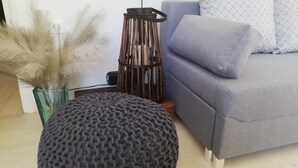 Un salon avec un canapé gris, des coussins à motifs, un pouf rond, un grand lampadaire et un vase contenant des plumes d’herbe des pampas.