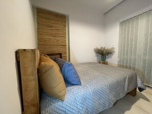 A bedroom with a bed, a wooden headboard, a bedside table with a vase of dried plants, and a window with blinds. - Hidden Gem in city’s heart (Χανιά)