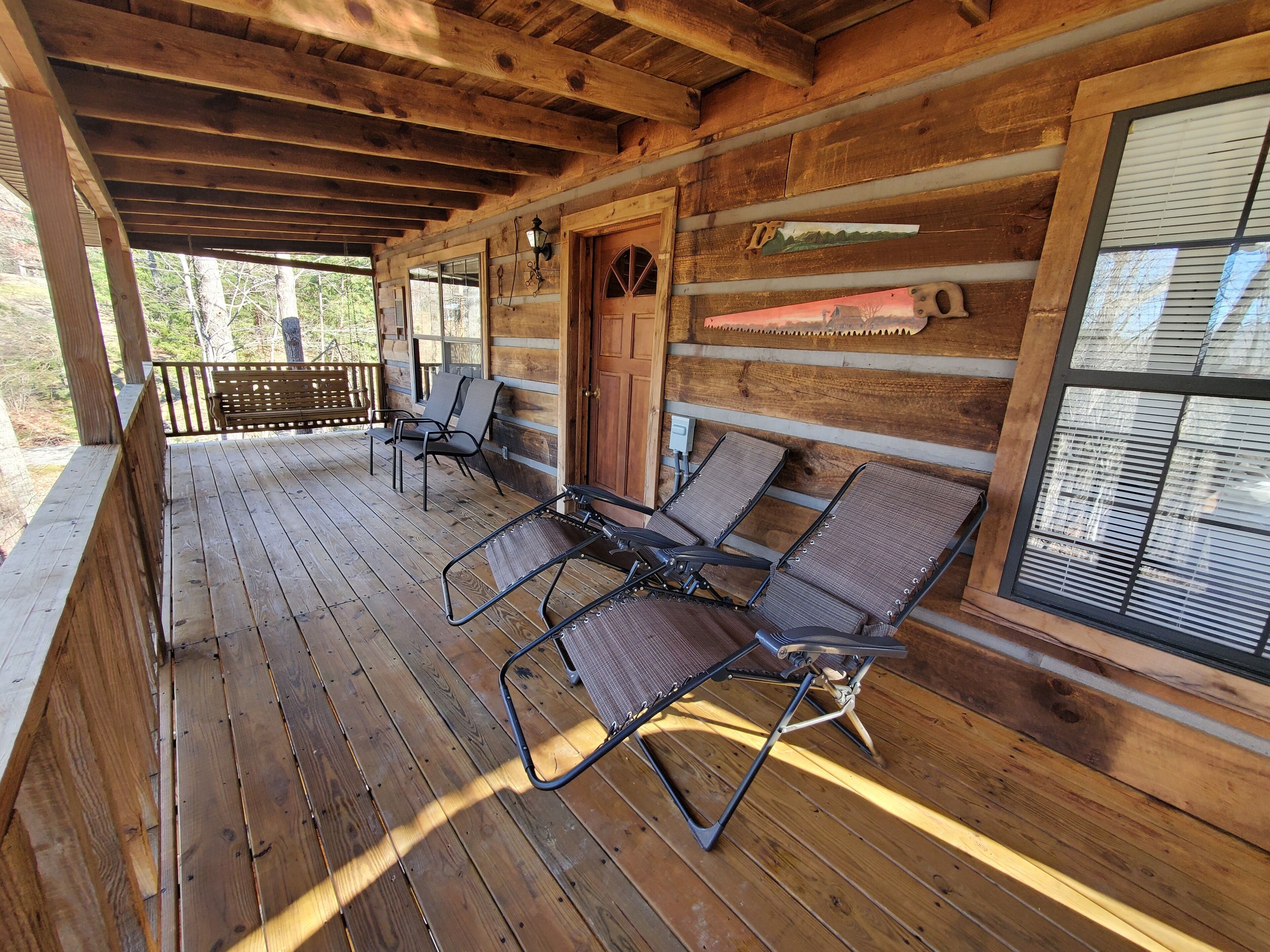 Een houten hut met een veranda, twee lounge stoelen, een deur en een raam met zonwering.