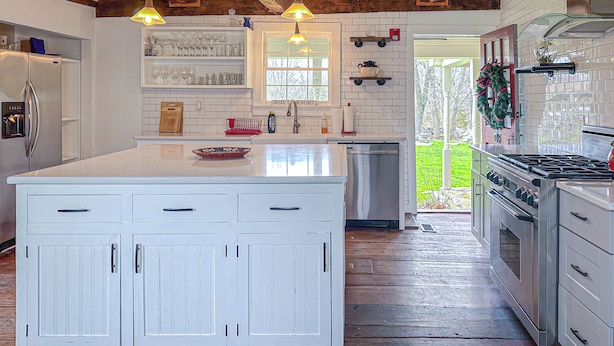 A kitchen with a large island, wooden beams, white cabinetry, and a view to the outside. - Coastal Antique farmhouse  (North Stonington)
