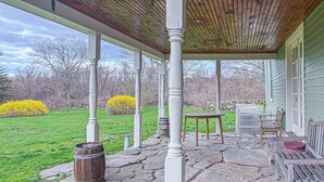 A covered porch with stone flooring, wooden columns, a table, and chairs. - Coastal Antique farmhouse  (North Stonington)