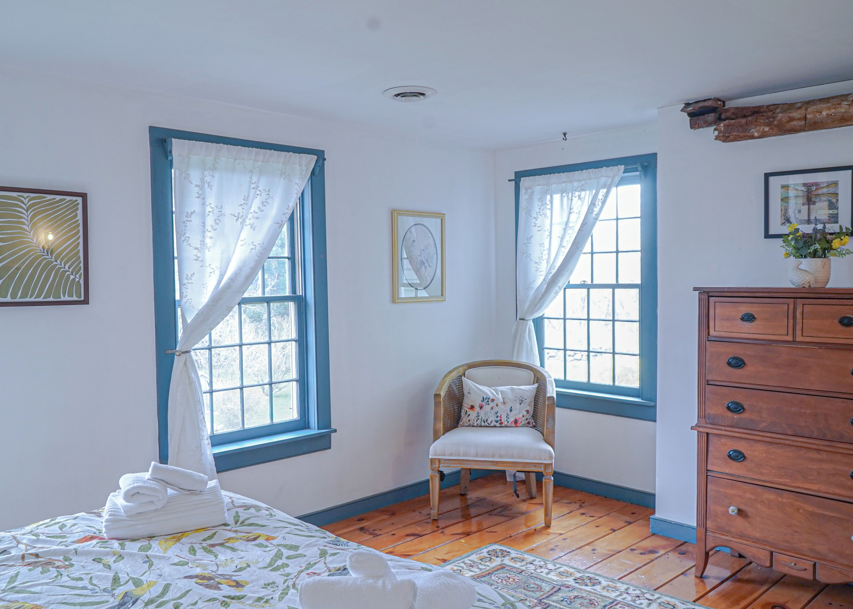 A bedroom with two windows, a wooden dresser, a chair, and a bed with a floral bedspread.