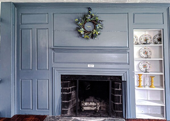 A fireplace with a blue mantel, a decorative wreath, and a shelf with plates and candles.