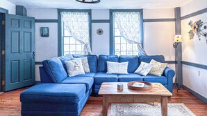 A room with a blue sectional sofa, a wooden coffee table, and a chandelier. - Coastal Antique farmhouse  (North Stonington)