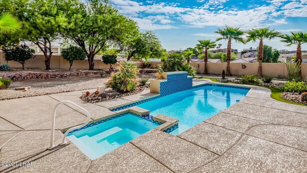 Ein Pool mit blauem Mosaikrand, umgeben von einem angelegten Garten mit Palmen und blauem Himmel.
