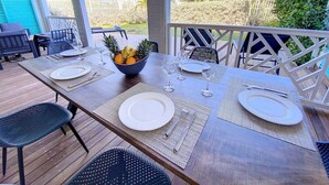 Un área de comedor al aire libre con una mesa de madera dispuesta para cuatro personas, rodeada de sillas y un bol de fruta en el centro.