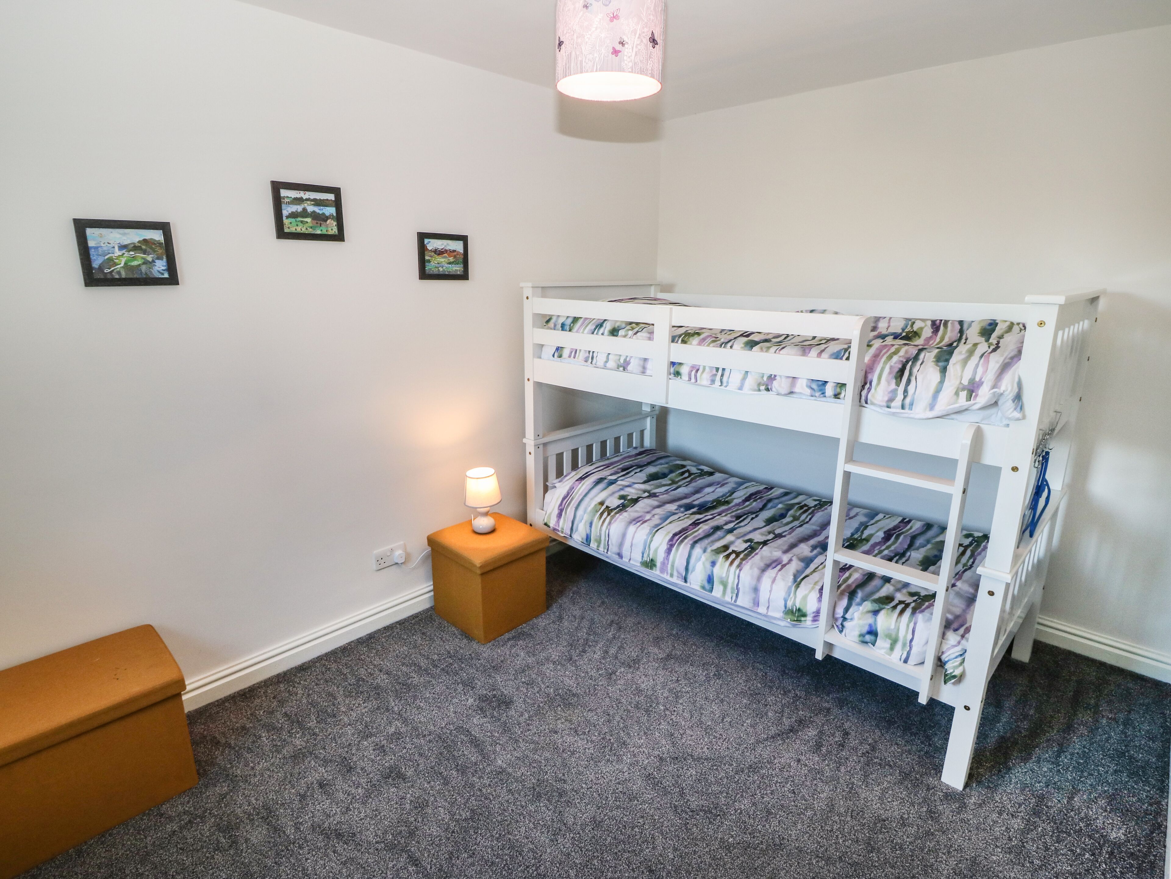 A child's bunk bed with a nightlight, a small wooden stool, and three framed pictures on the wall.