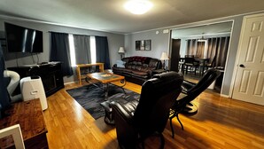 A living room with a sofa, a coffee table, a TV, and a dining area in the background. - Downtown Hub - Dog Friendly (Redmond)