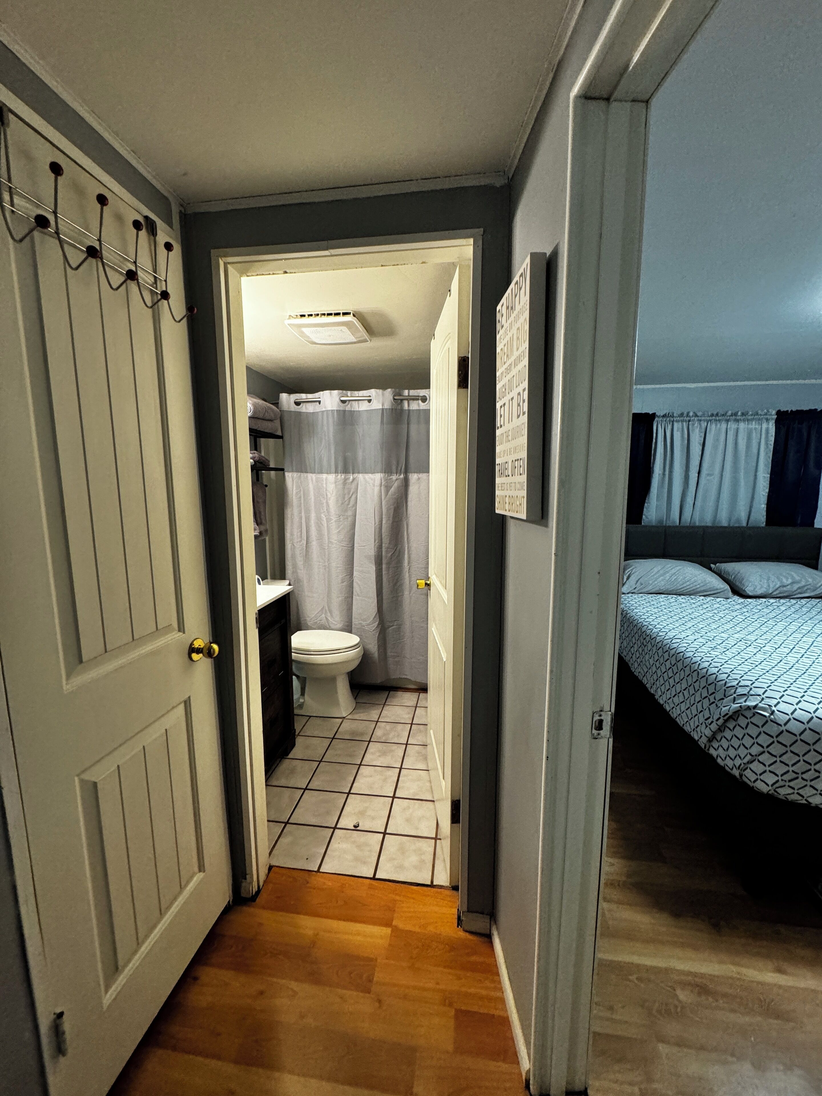 Un couloir étroit mène à une salle de bain équipée de toilettes, d’un rideau de douche et d’un lit avec une literie à motifs.