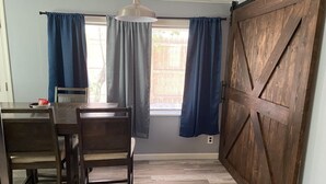 A room with a wooden dining table and chairs, a large window with blue curtains, and a wooden barn-style door. - Downtown Hub - Dog Friendly (Redmond)