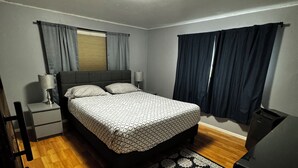 A bedroom with a bed, bedside tables, a lamp, a window with curtains, a wooden floor, and a ceiling light. - Downtown Hub - Dog Friendly (Redmond)