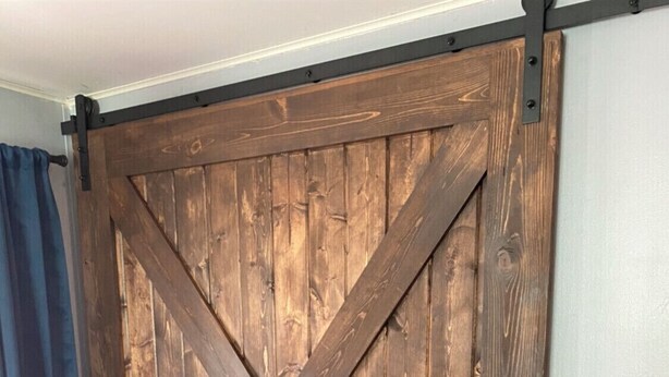 A large wooden barn-style sliding door in a room with light-colored wooden flooring and a blue curtain. - Downtown Hub - Dog Friendly (Redmond)