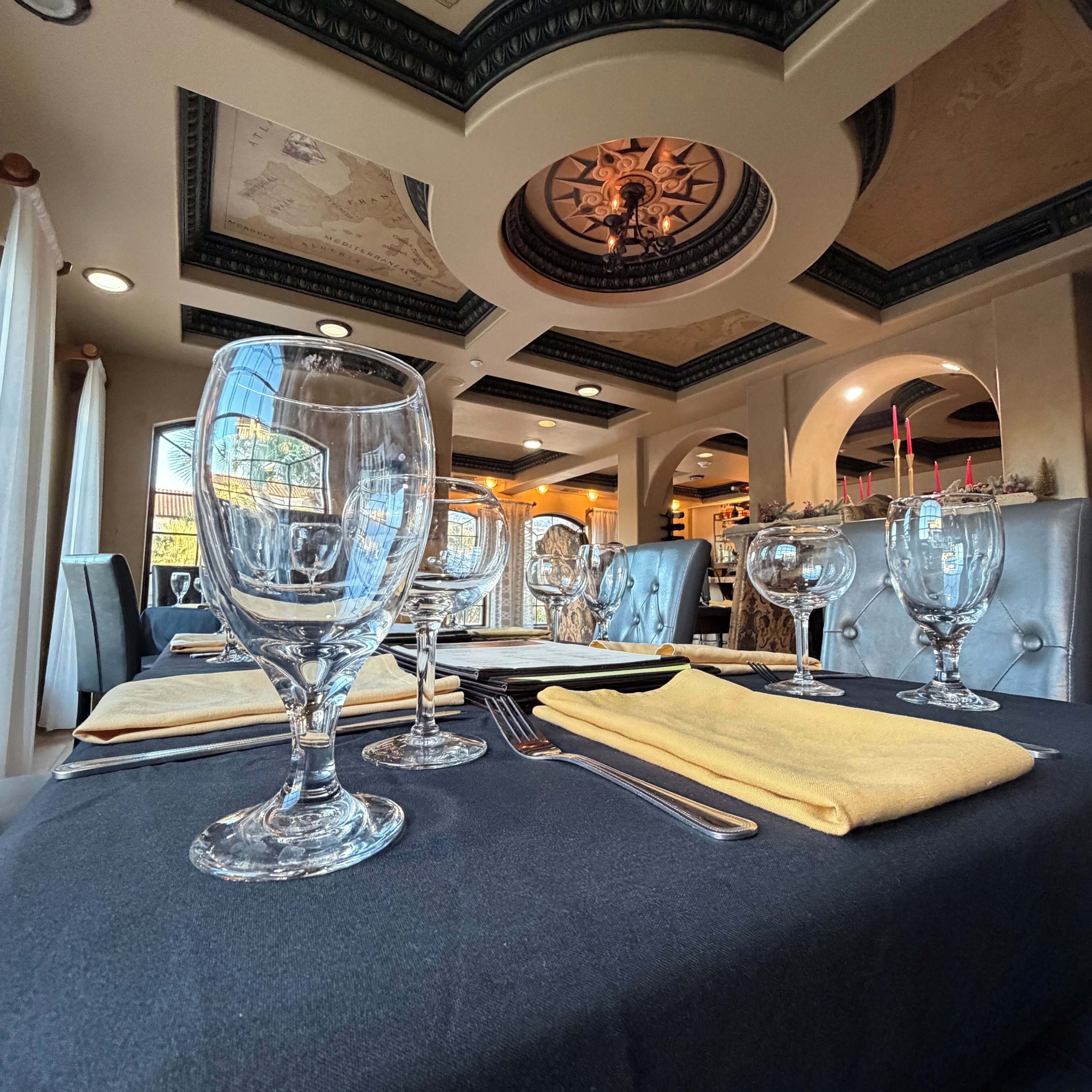 A dining area with tables set for a meal, featuring clear glassware and a dark tablecloth.
