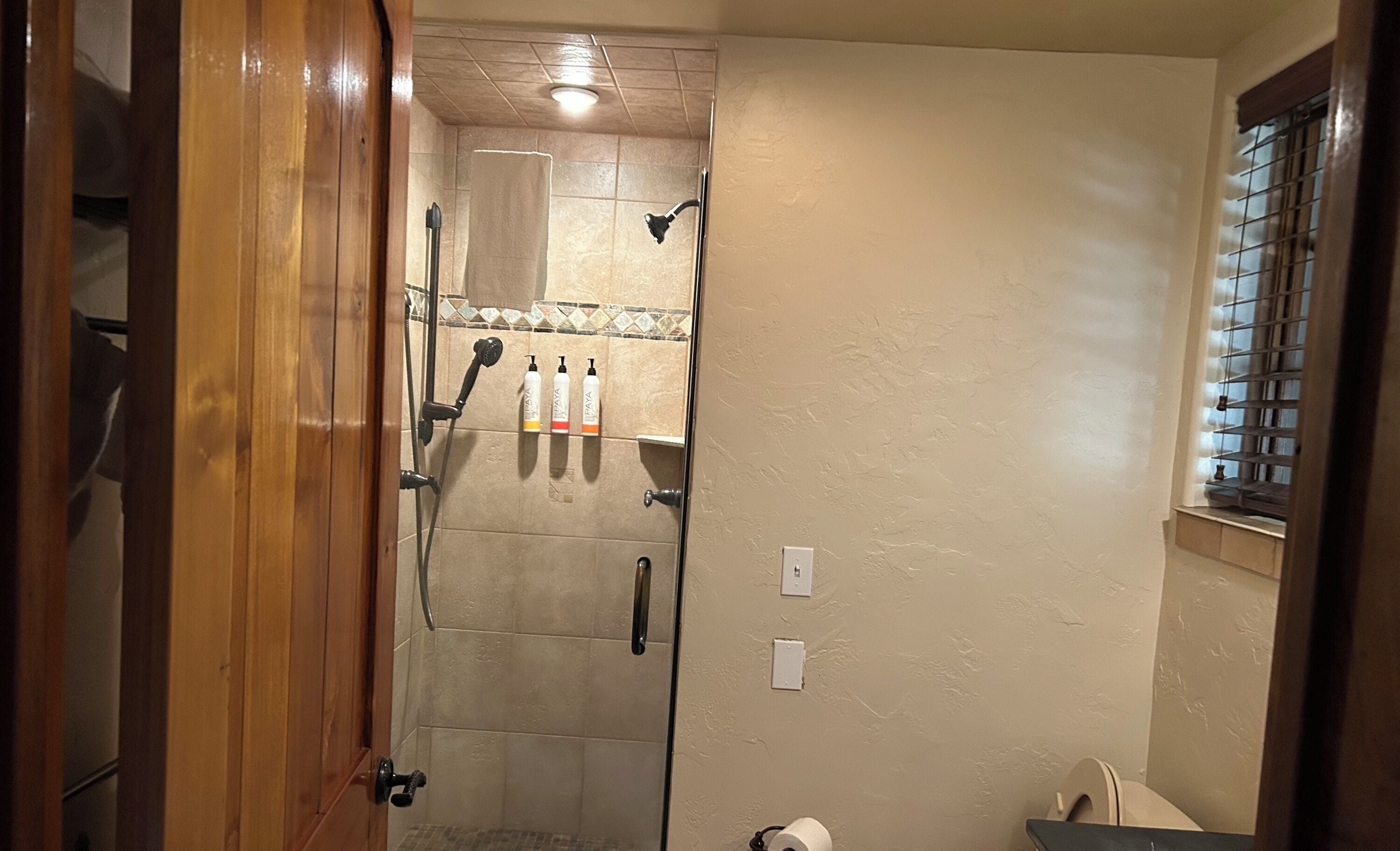 Une salle de bain avec une douche, des toilettes et une fenêtre équipée de stores.