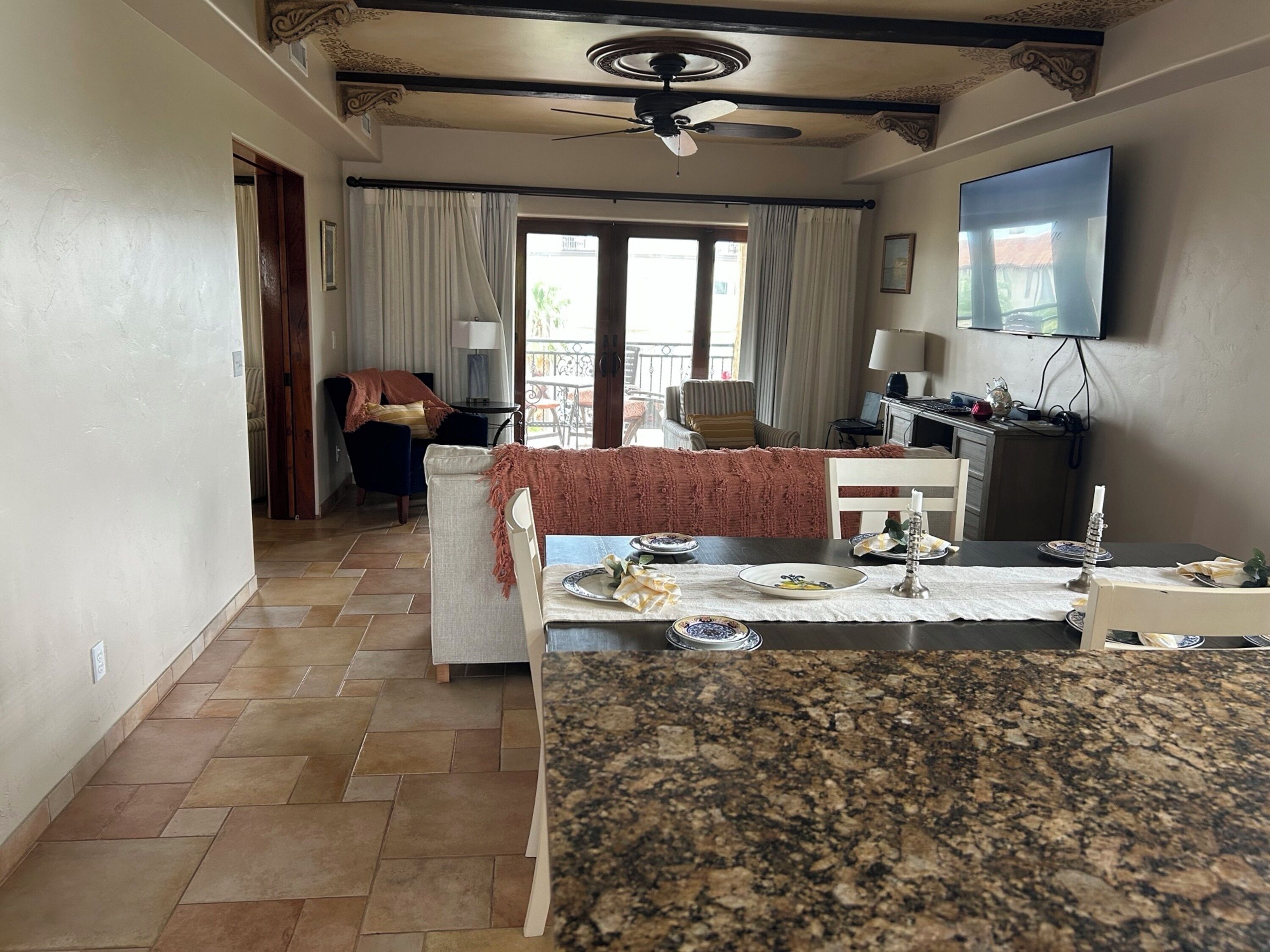 Un coin repas doté d’un plan de travail en granit, d’une table à manger dressée avec des assiettes et d’un ventilateur de plafond.