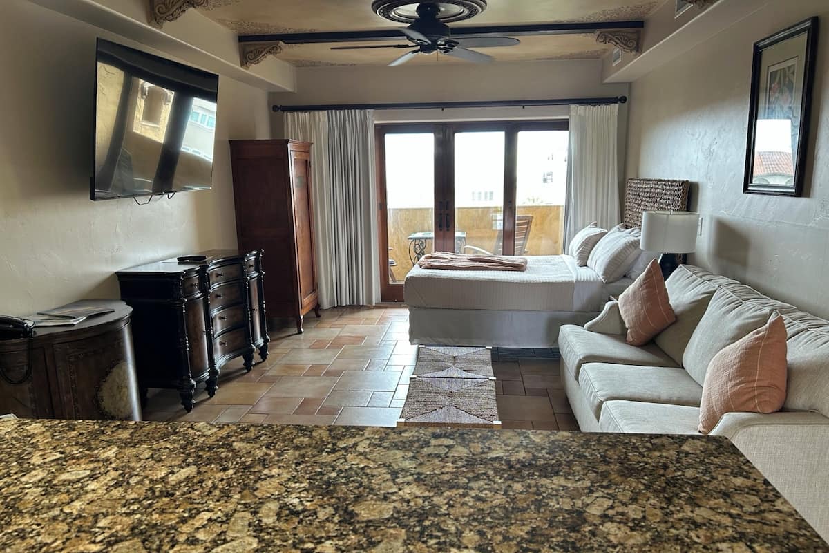 A spacious living room with a large bed, a sofa, a TV, and a ceiling fan.