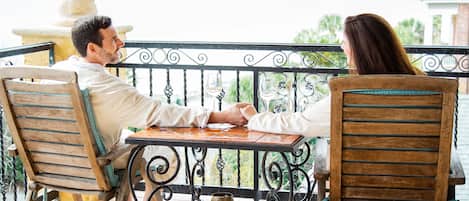 Un couple est assis à une table sur un balcon, d’où l’on a une vue sur la mer.