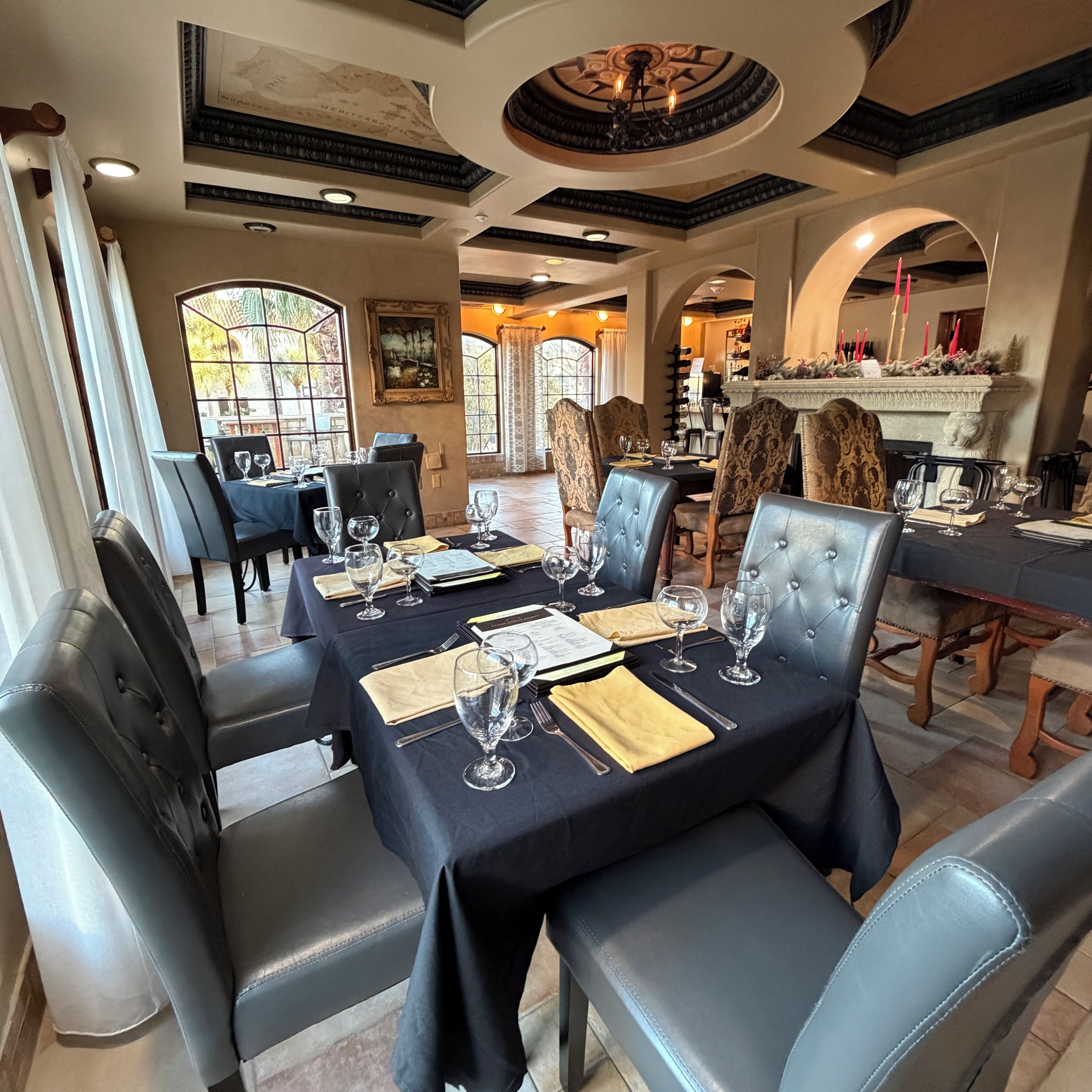 A dining area with black tablecloths, leather chairs, and wine glasses set for a meal.